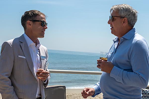 Two men talking with water in the background.