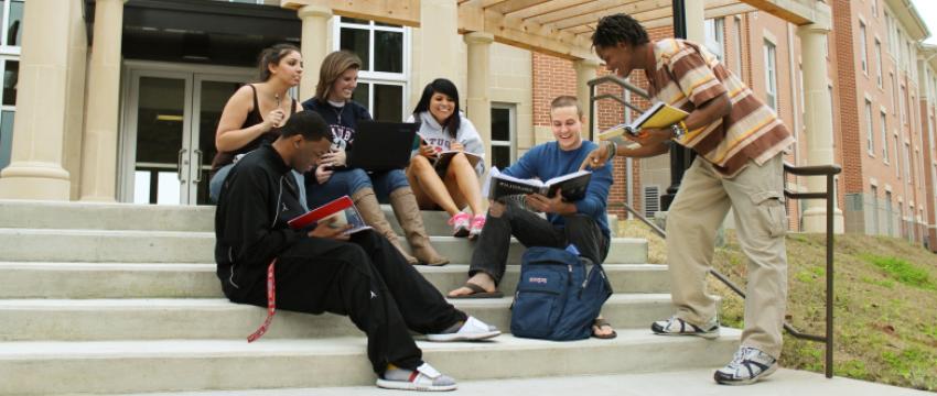 一群学生坐在美国宿舍外的台阶上，拿着书和笔记本电脑.